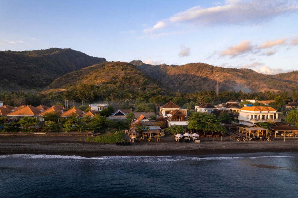 breathtaking sunrise illuminating houses on black sand beach in amed, bali