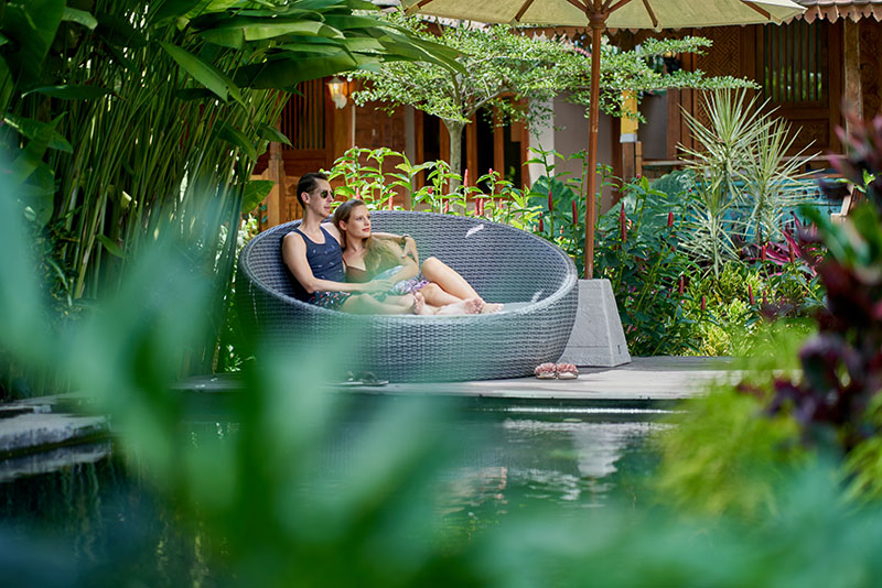 young couple lounging in modern chair near luxurious pool of tropical hotel and spa in bali