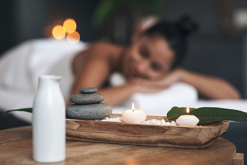  closeup shot of a tranquil spa arrangement with a woman laying on a treatment bed in the background